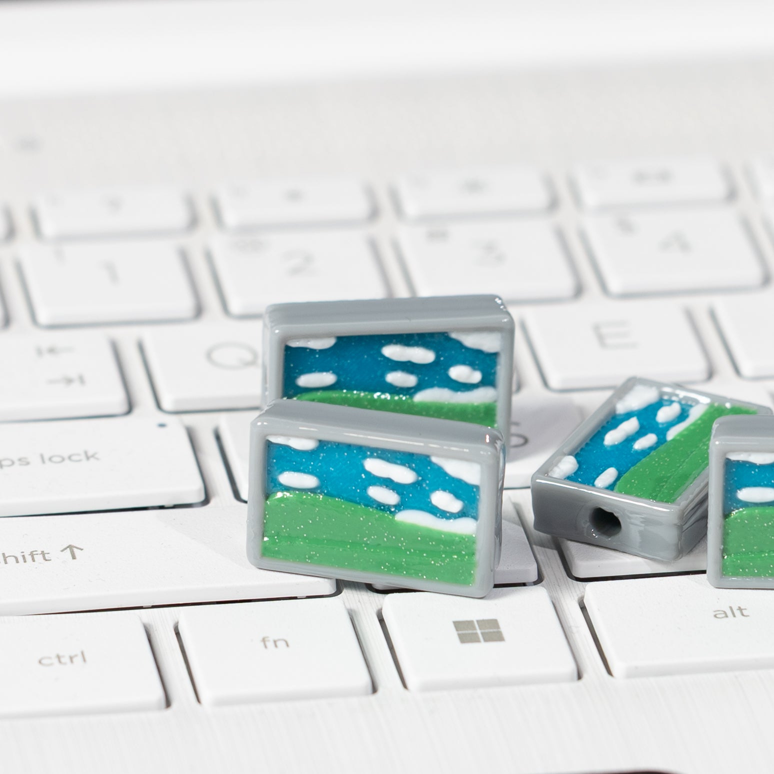 Two Windows Bliss kandi beads with blue sky and green hills propped on a white keyboard