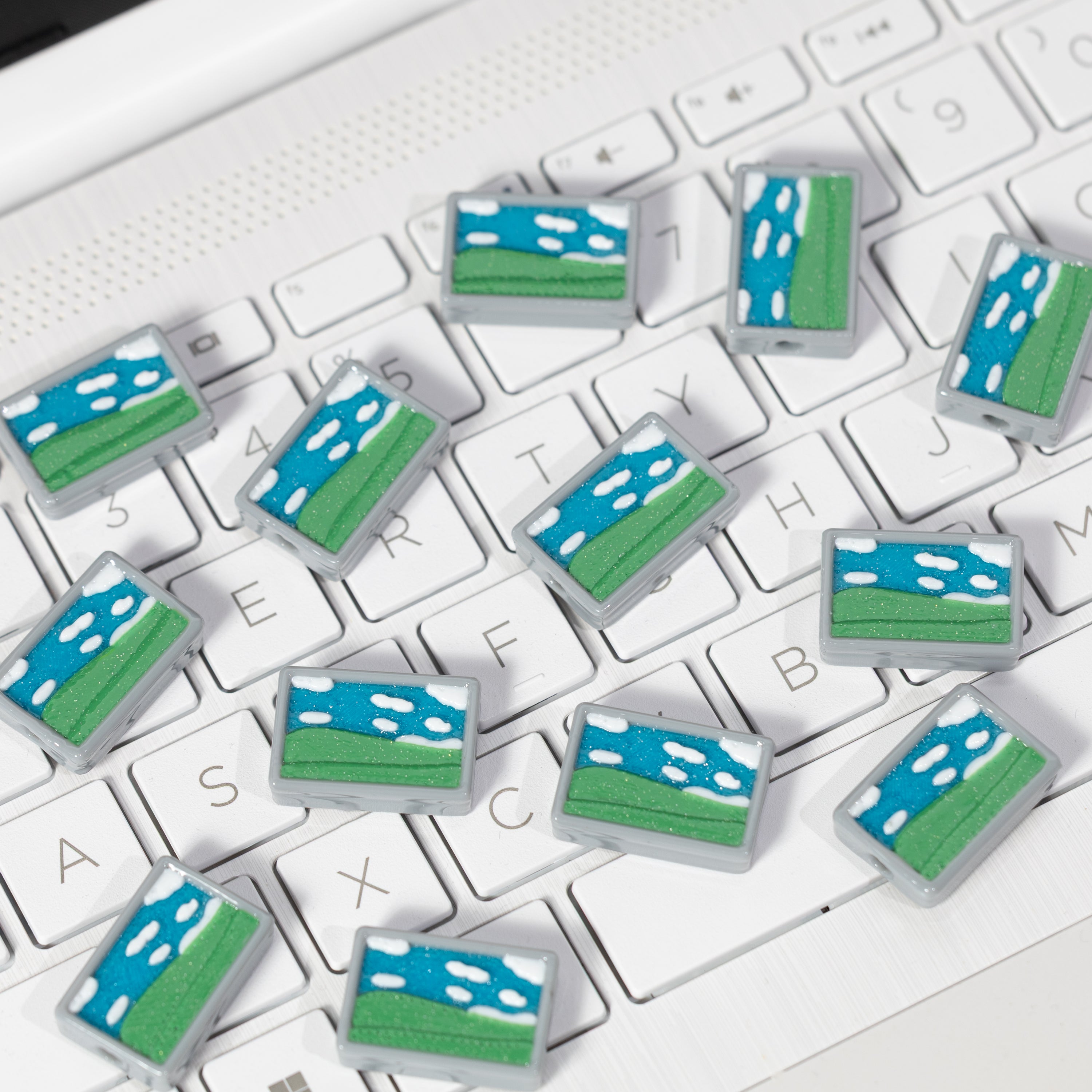 A dozen blue and green Windows Bliss kandi beads scattered across a white keyboard