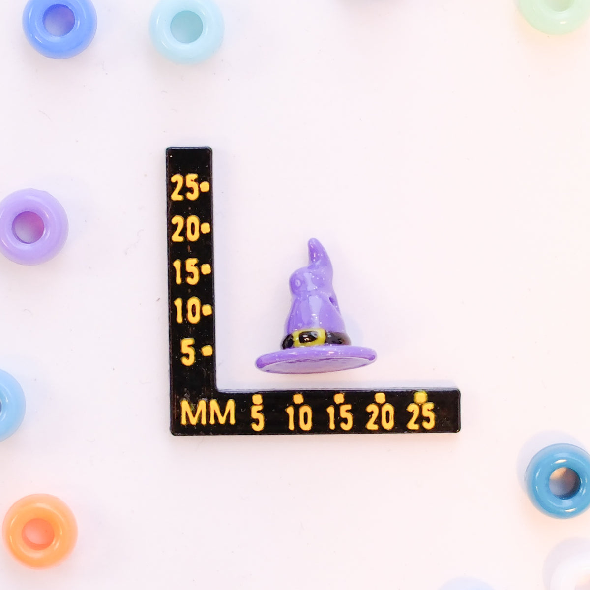 Size guide: a witch hat kandi bead beside a millimeter ruler for scale