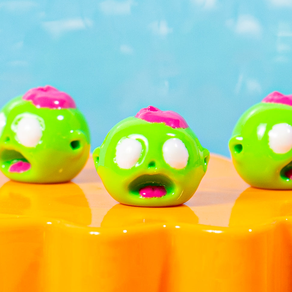 Close-up of green zombie head kandi beads with pink brains and white eyes on an orange riser