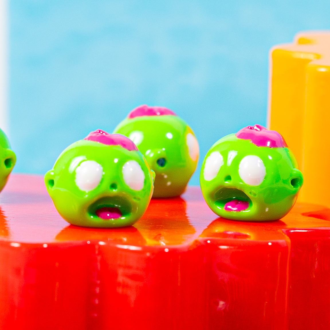 Three zombie head kandi beads with open mouths on a glossy red riser