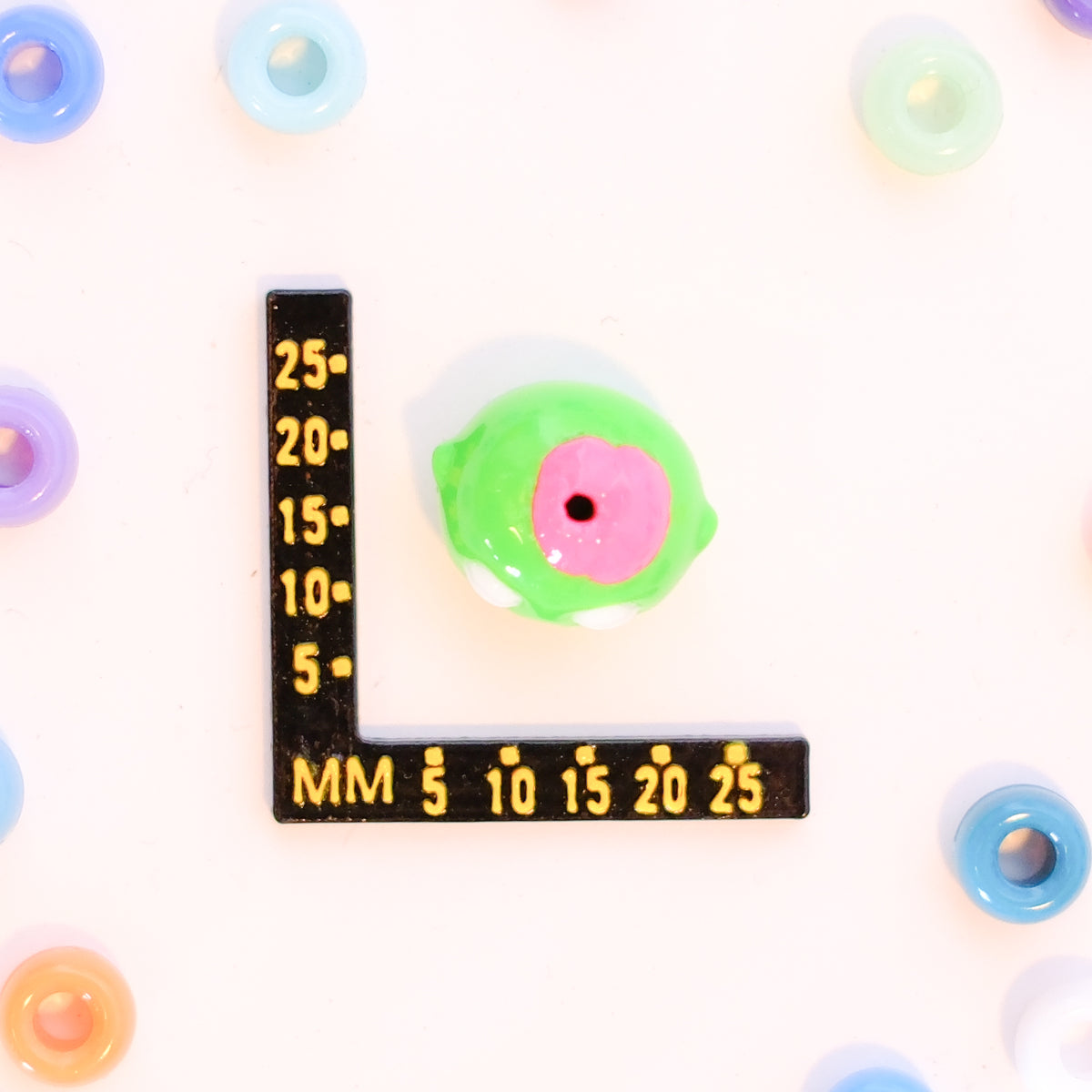 Size guide: a zombie head kandi bead beside a millimeter ruler for scale, top hole visible