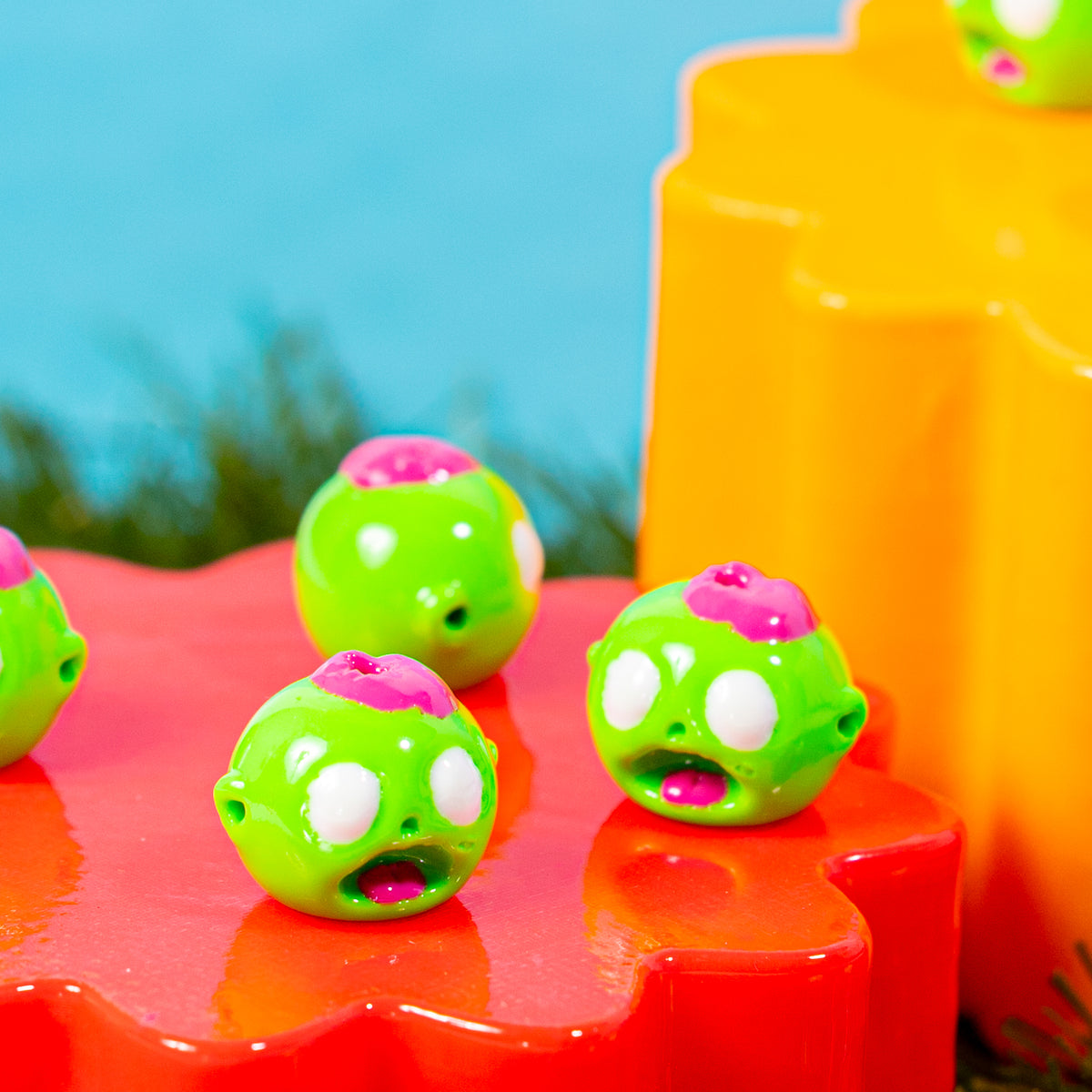 Green zombie head kandi beads grouped on a red riser in front of an orange block
