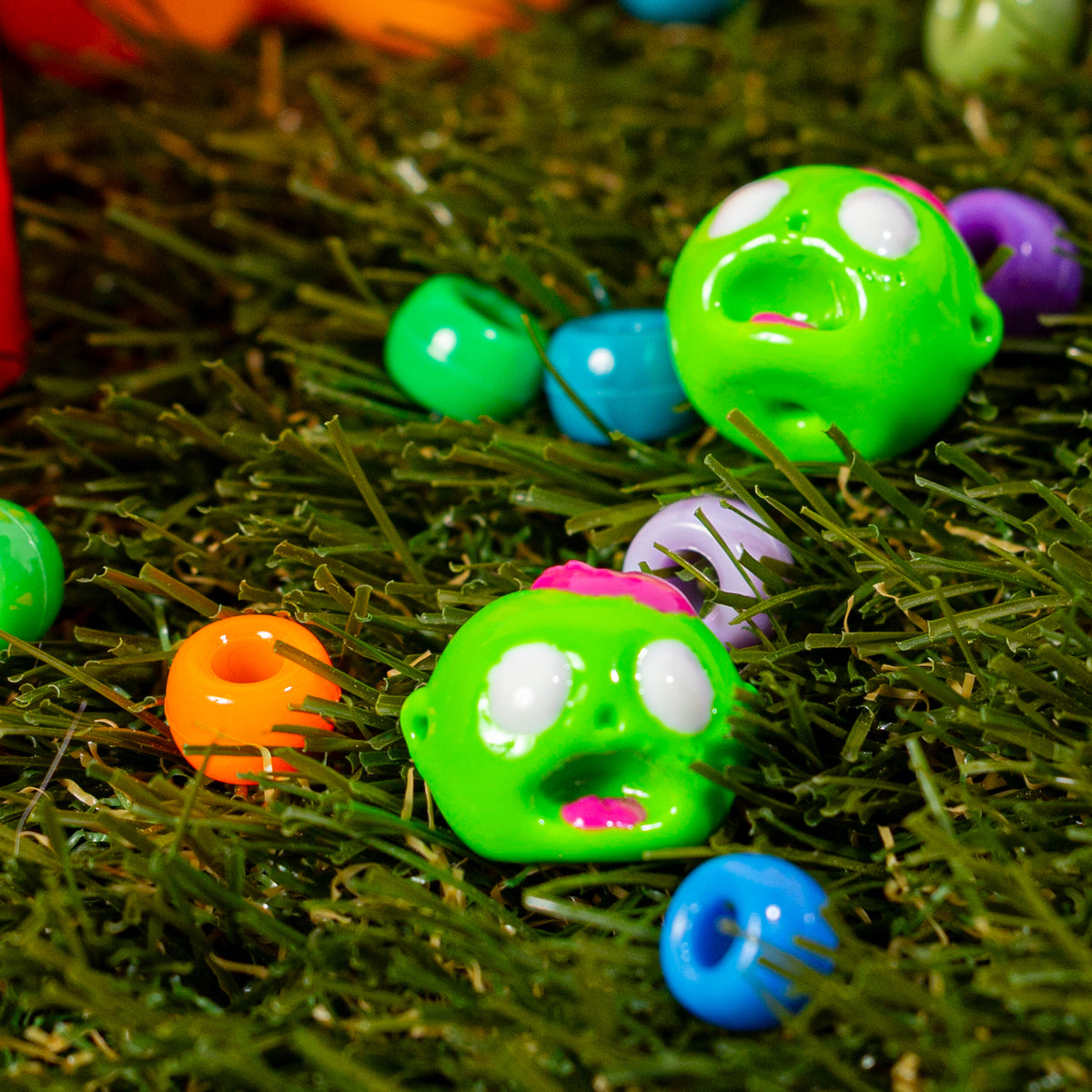 Zombie head kandi beads in green grass with colorful beads, side hole visible